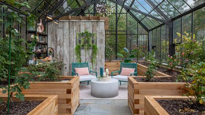 A large residential greenhouse with seating area and natural wood raised garden beds