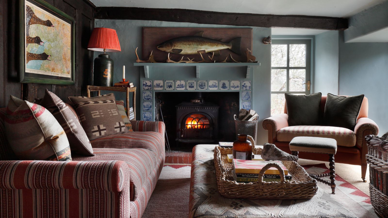 small cabin style living room with a delft tile fireplace, log burner, pattern mixed furniture and a large fish wall art above the fireplace