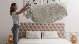 Woman putting a bedsheet on the bed with two bedside tables on either side