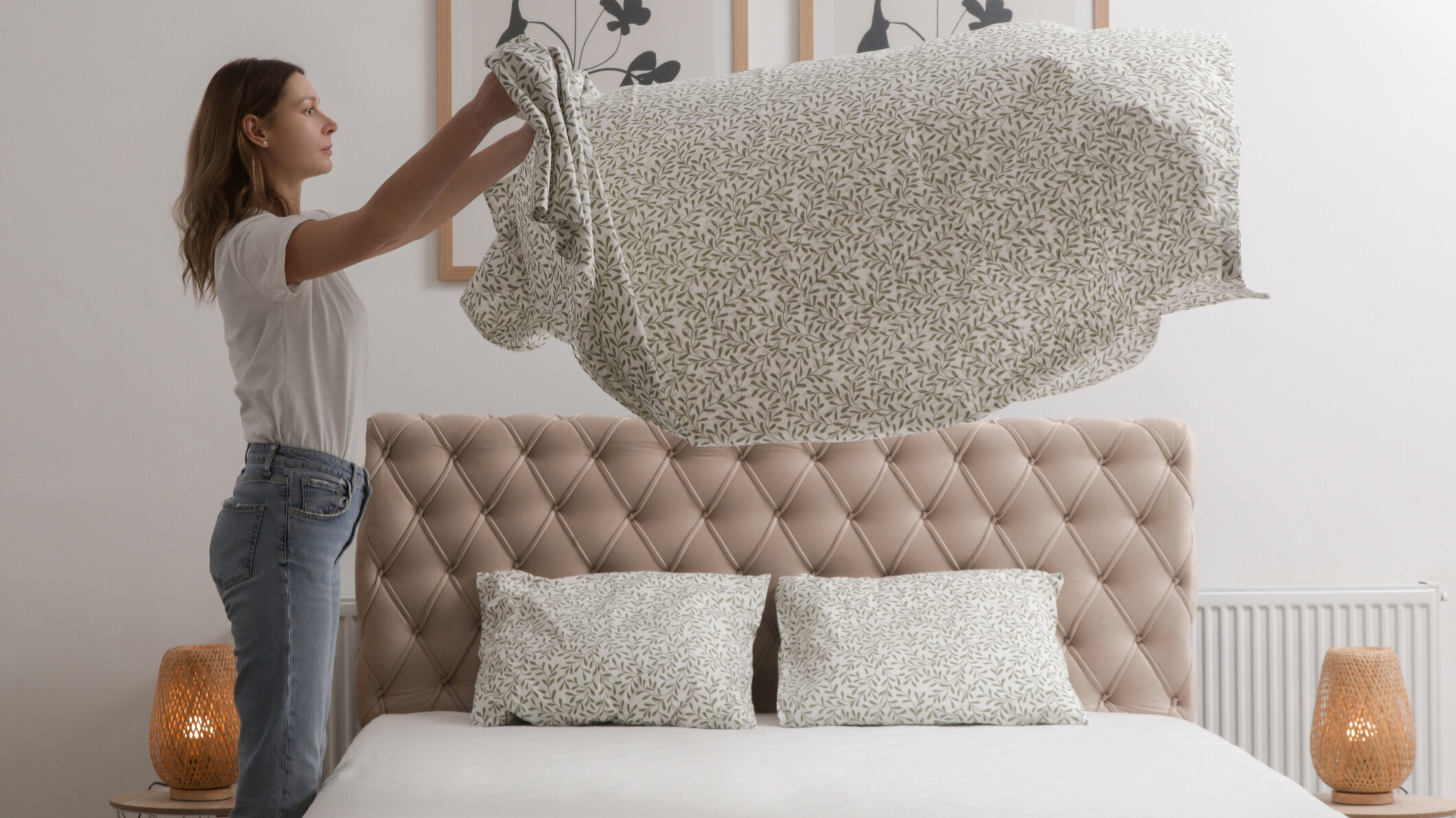 Woman putting a bedsheet on the bed with two bedside tables on either side