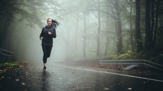 Young athletic woman running through misty woodland