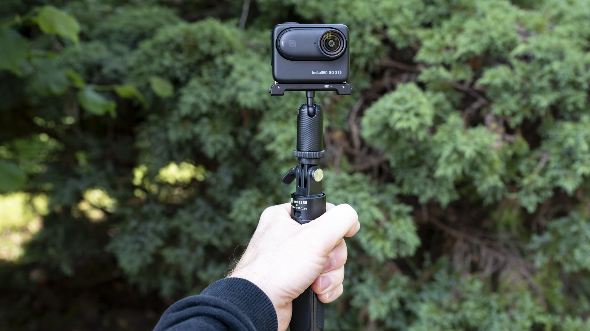 Insta360 Go 3S camera in its housing attached to a selfie stick, outdoors