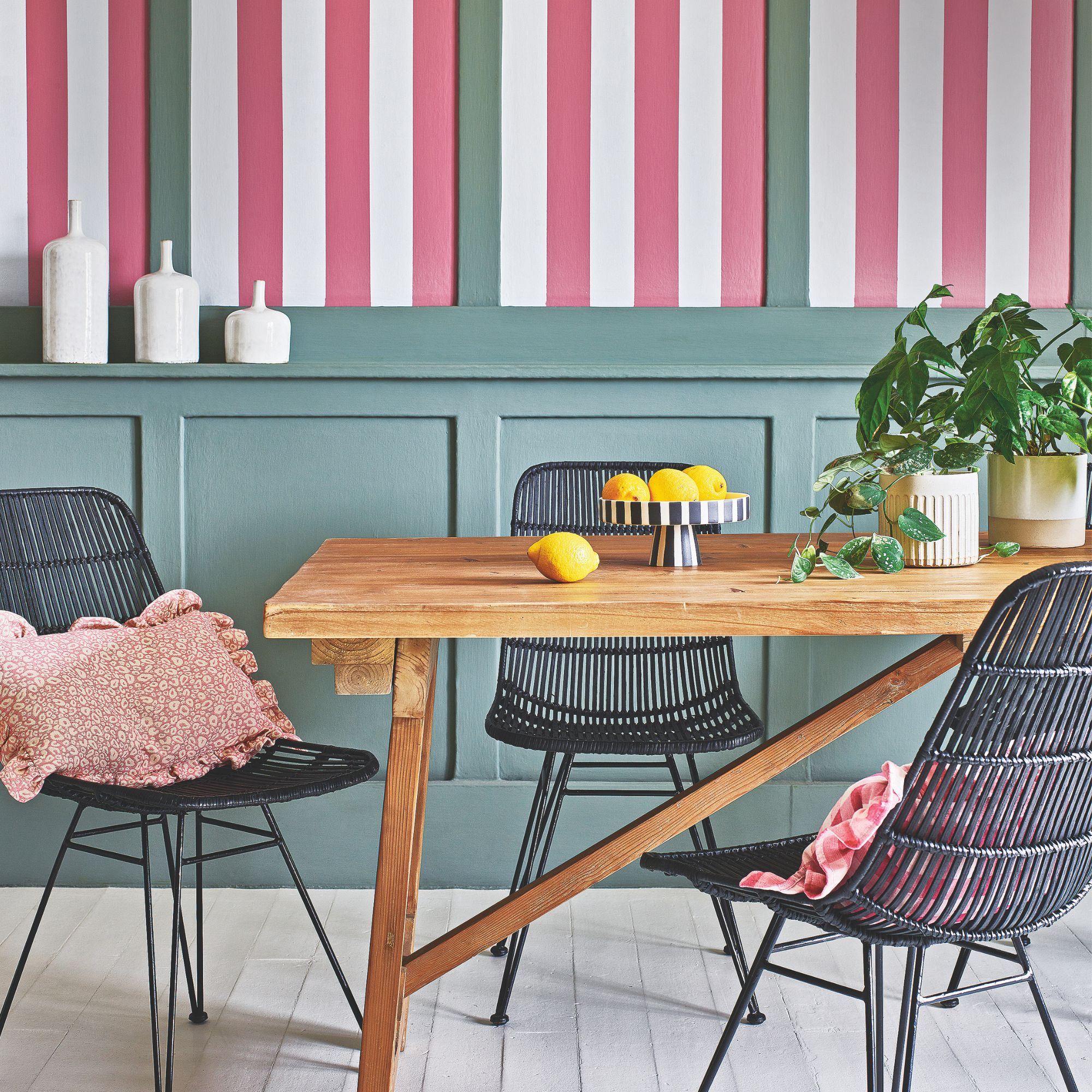 A wooden table against a statement wall with sage green panelling and red and white striped wallpaper