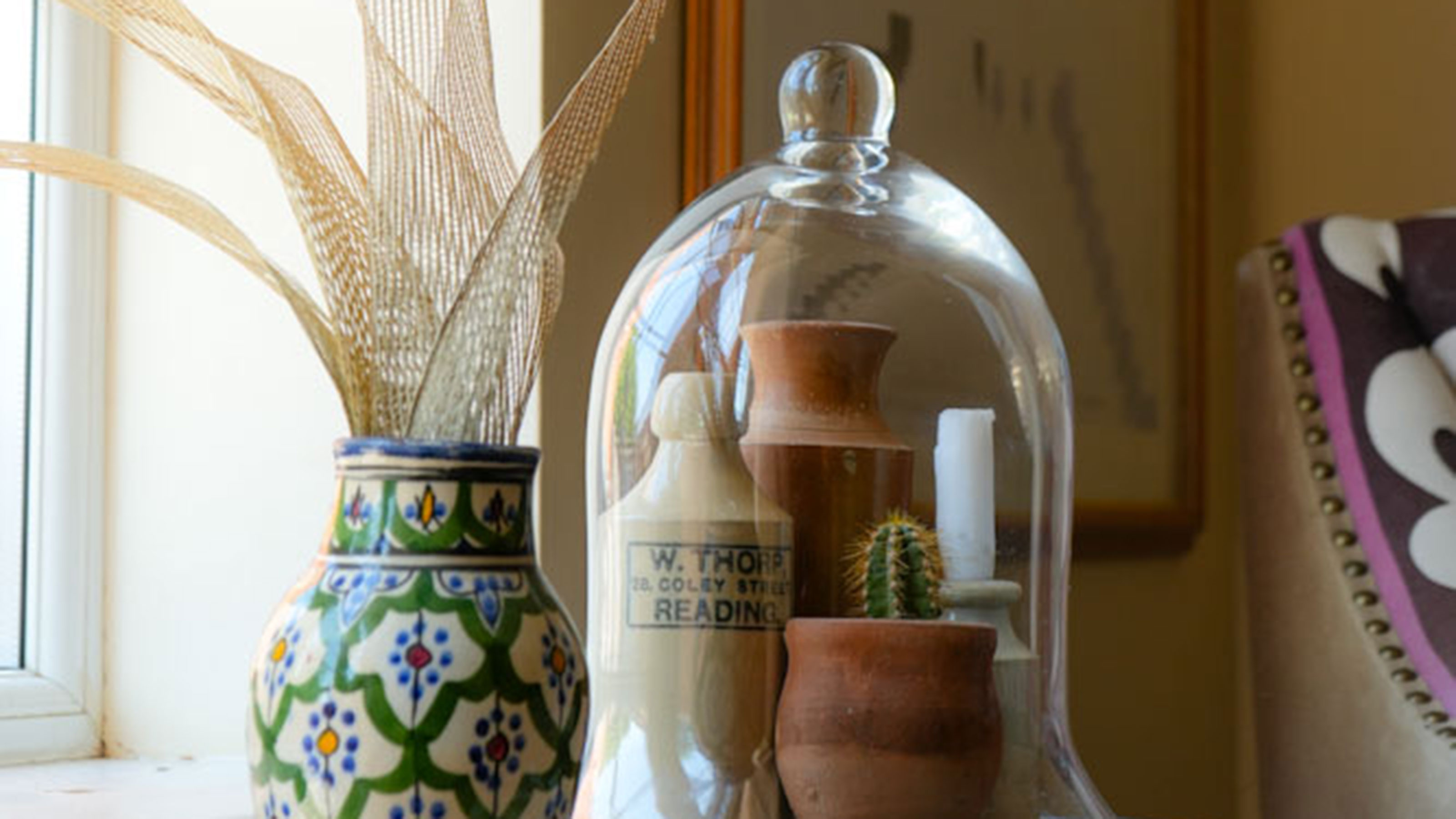 Ceramic jars and cactus under glass cloche beside patterned vase with fabric flowers