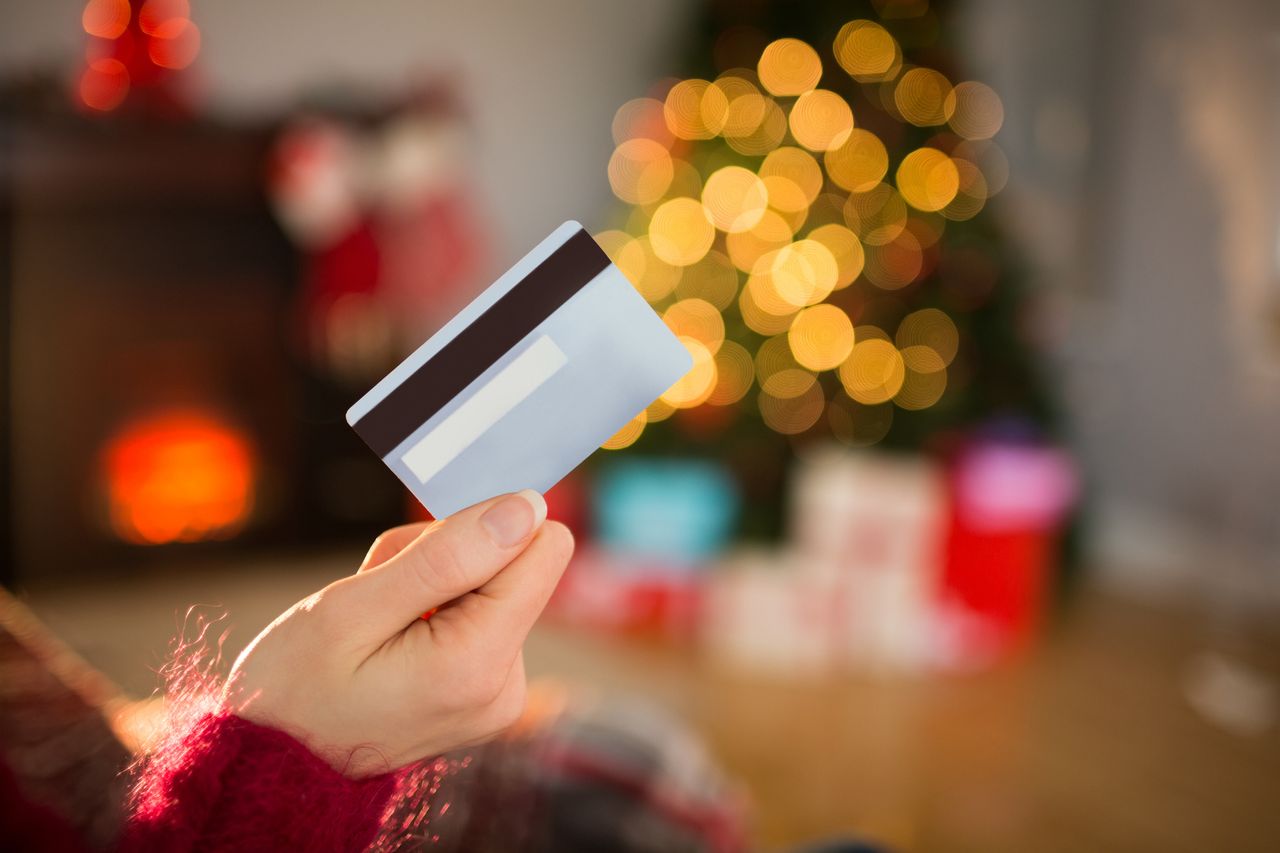 A woman&#039;s hand holds a credit card, with holiday lights in the background.