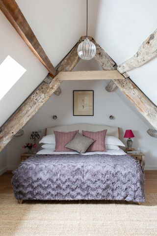 a loft bedroom with heavy timber frames on the ceiling, and a beige jute rug on the floor