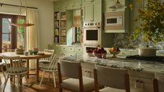 a bright mint green large kitchen with bold marble countertops, an island and a small round breakfast table and chairs