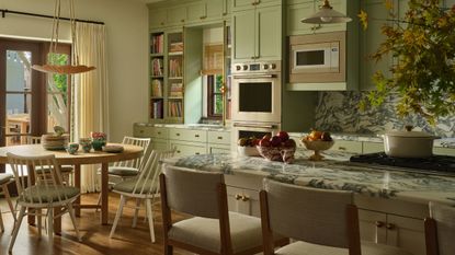 a bright mint green large kitchen with bold marble countertops, an island and a small round breakfast table and chairs