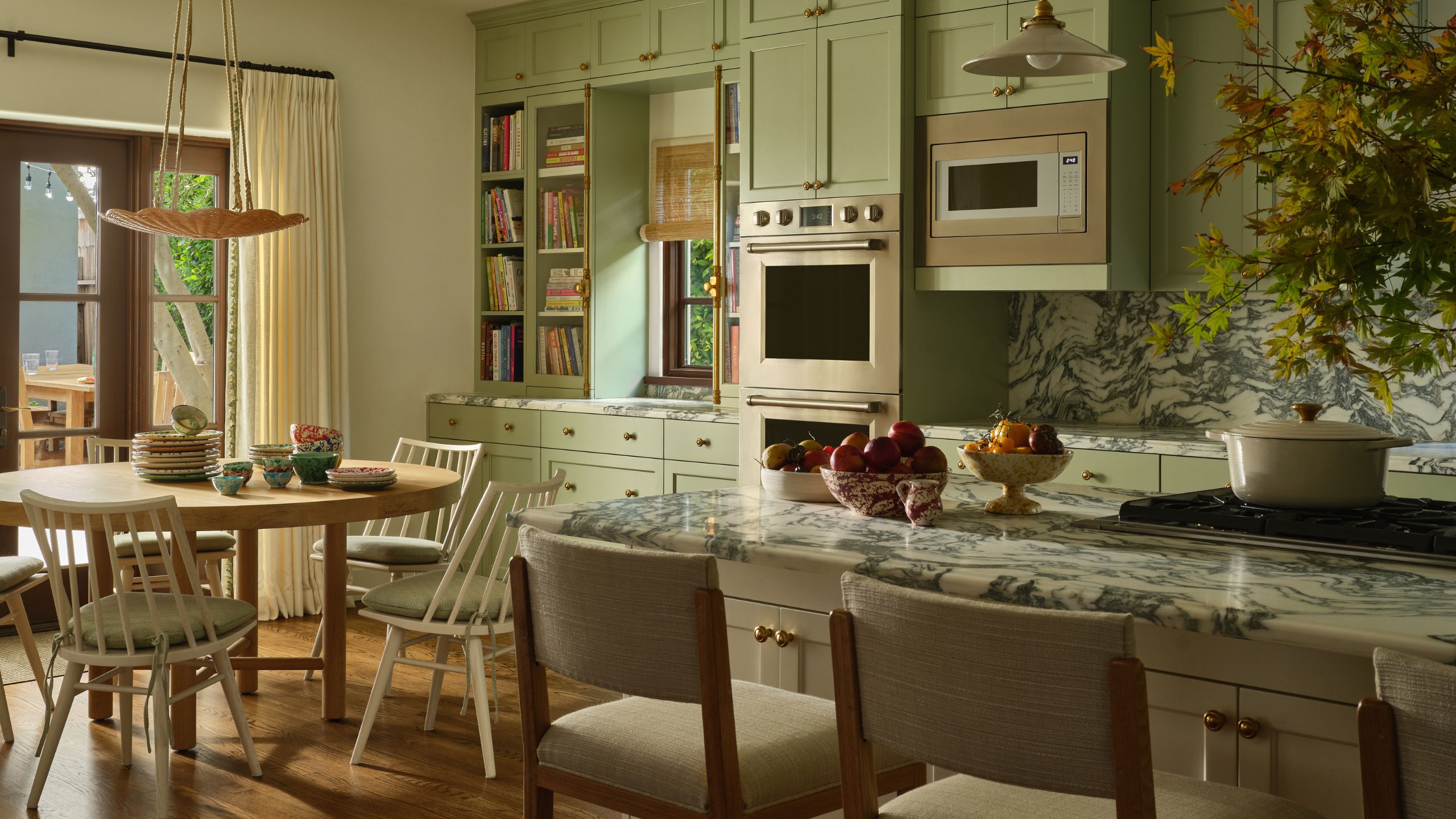 a bright mint green large kitchen with bold marble countertops, an island and a small round breakfast table and chairs