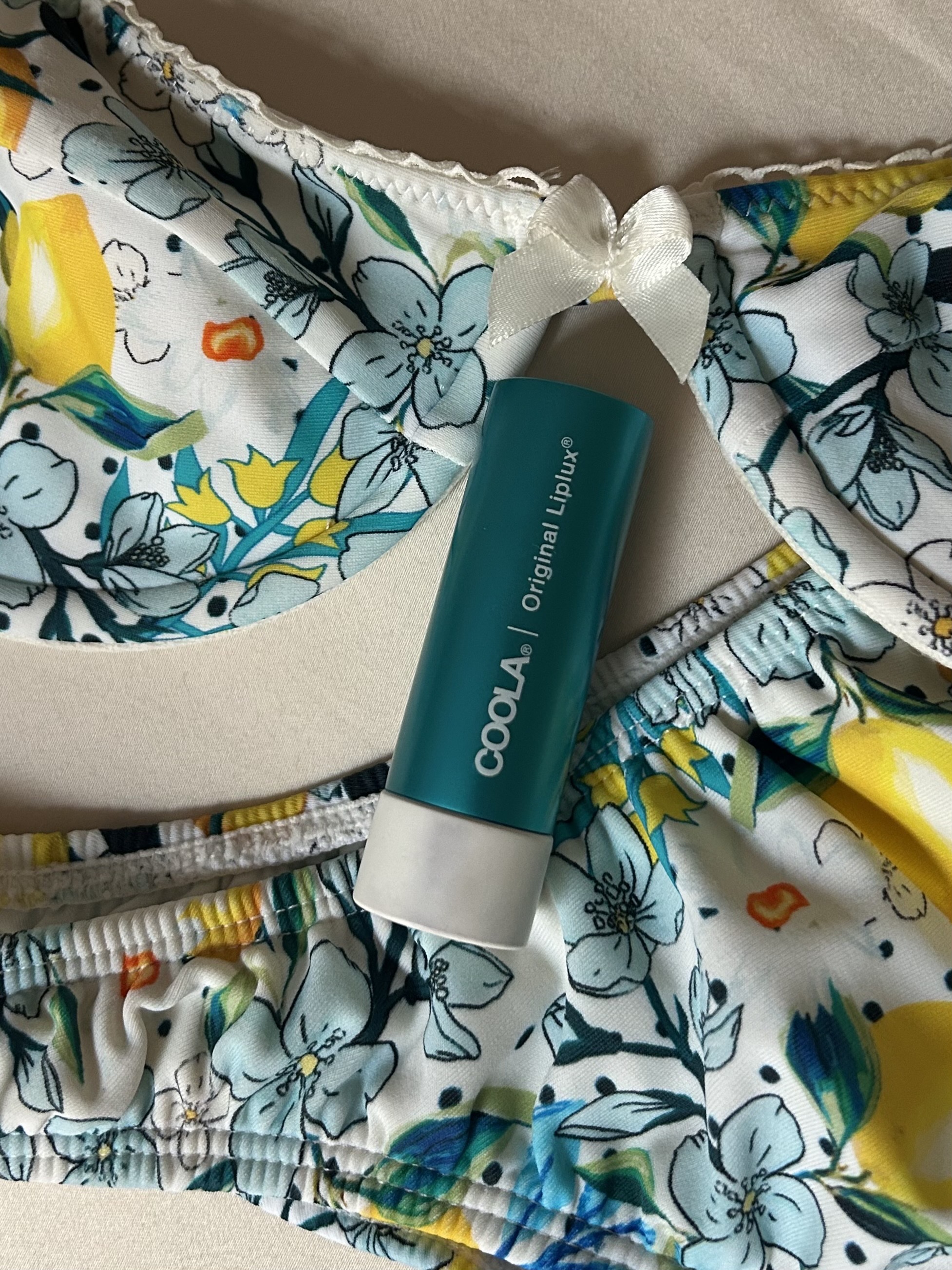 Image of Coola's Organic Liplux Classic Sunscreen Lip Balm SPF 30 lying on top of a bathing suit.