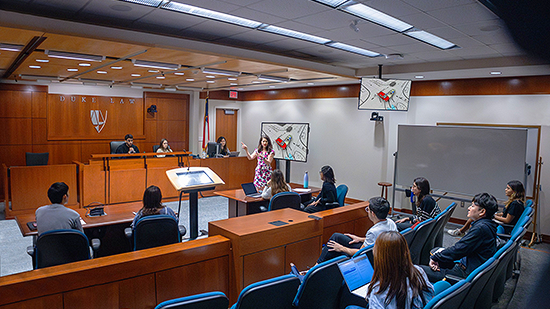 A woman leads a mock discussion at Duke Law School&#039;s courtroom. 