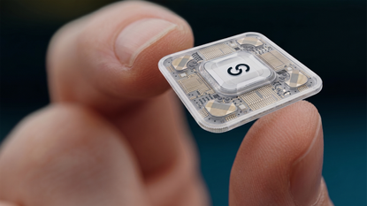 A close up of someone's hand holding a small electronic circuit chip with the letter S on it in the middle
