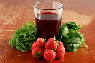 A glass of beetroot juice behind strawberries