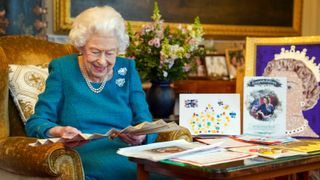 Queen Elizabeth II looks at a fan as she views a display of memorabilia from her Golden and Platinum Jubilees in the Oak Room at Windsor Castle on February 4, 2022 in Windsor, England.