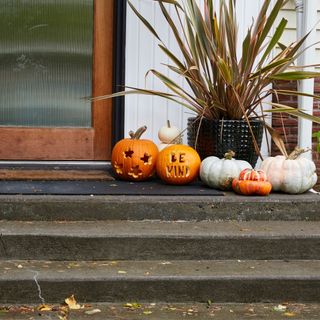 Halloween pumpkins carved with the words 'be kind' sat outside a modern house's front door
