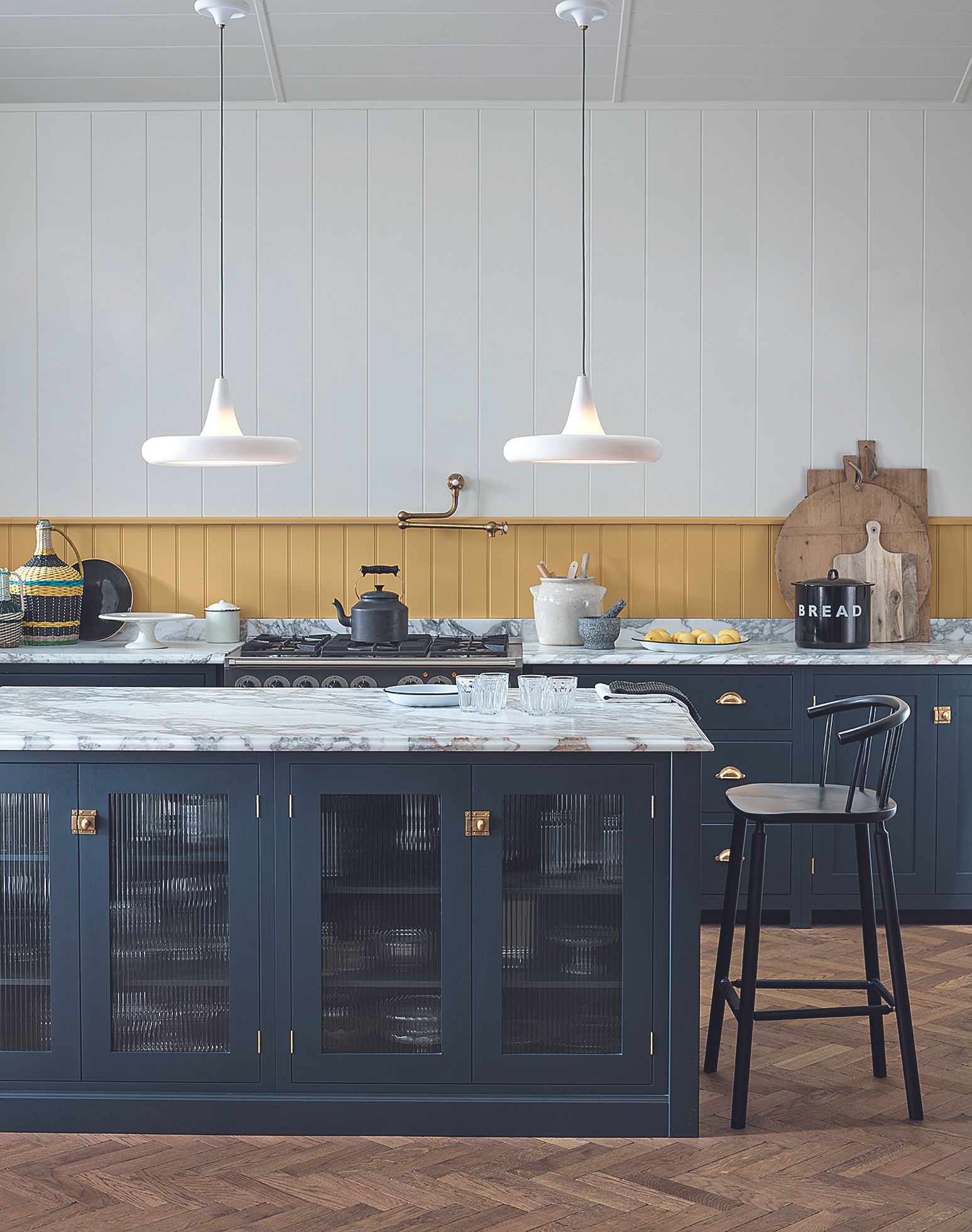 A marble island with dark blue cabinets and delicate white pendant lighting