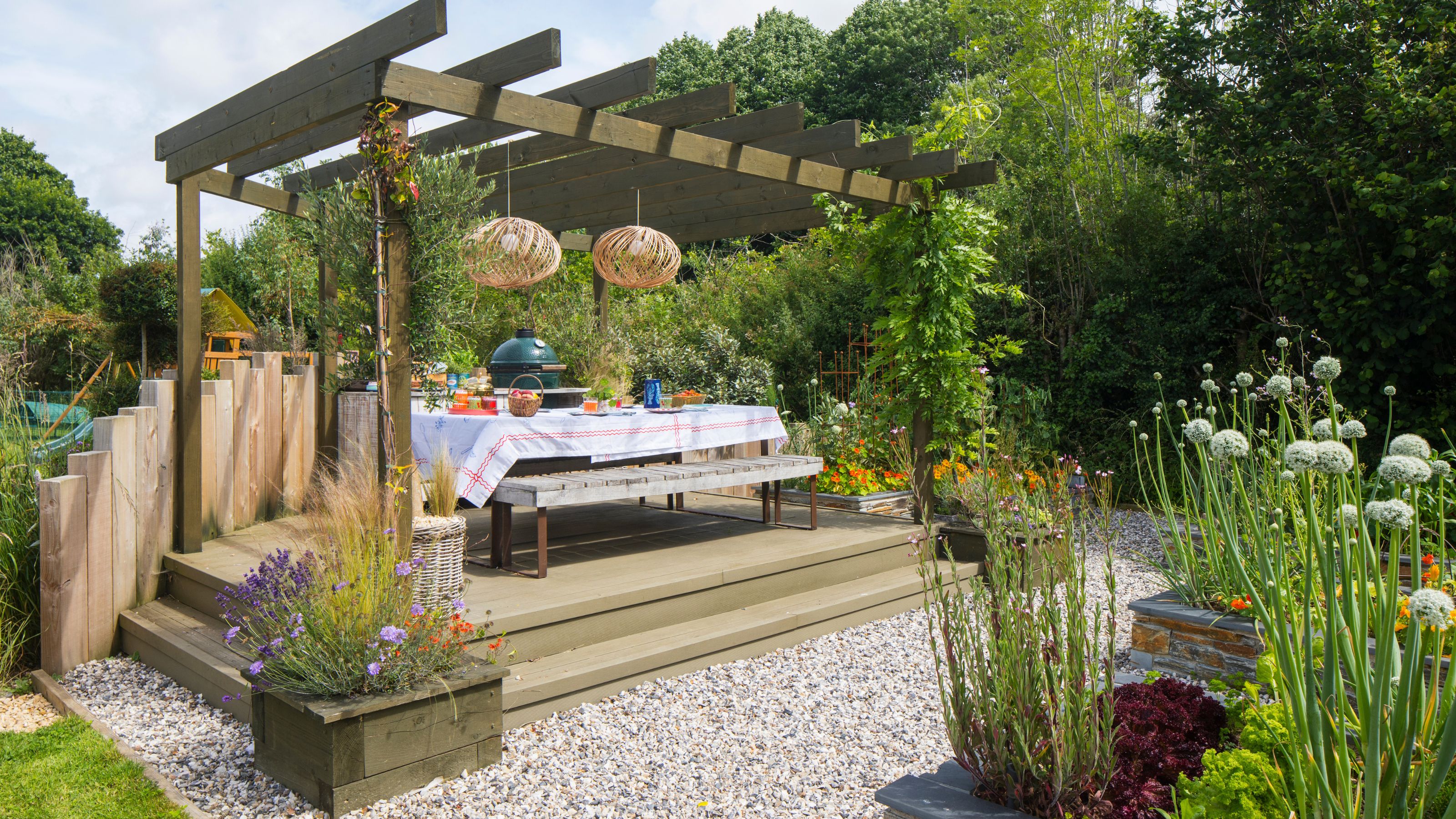 Outdoor area with gravel and wooden raised planters, and a raised decking area with a pergola above it