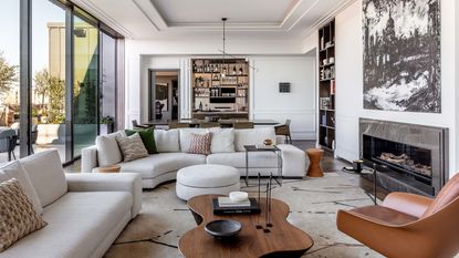  living room with white modular sofas, dining table, bar, bookcase, artwork, patterned rug, leather armchair, wooden coffee table