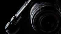A close-up shot of a Panasonic Lumix DMC GX7Y camera lens set against a dark background with the light focus highlights the logo and lens details