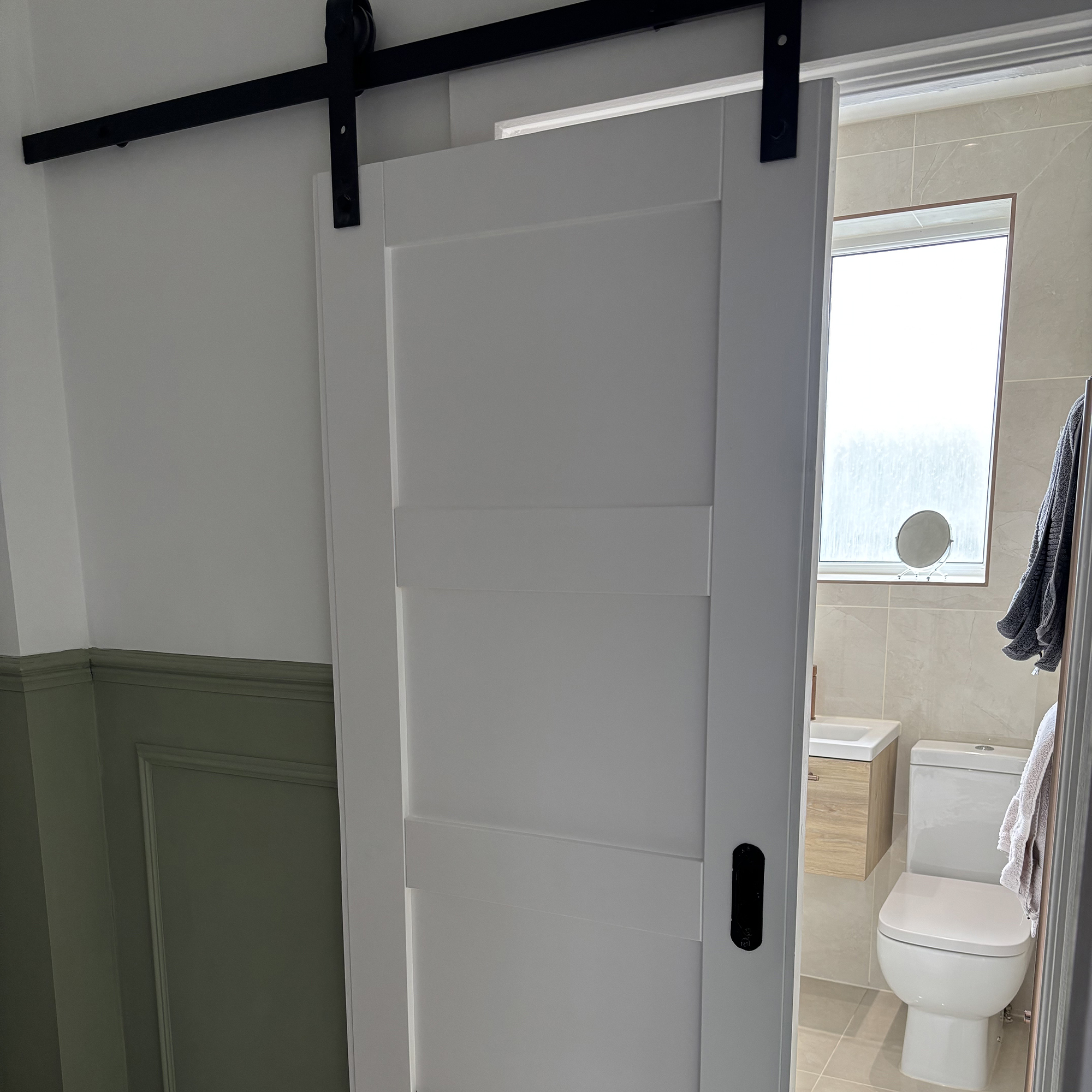 white sliding bathroom door slightly open to reveal a glimpse of a beige bathroom behind