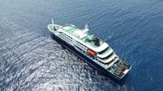 An aerial photo of a white cruise ship in the middle of a blue ocean.