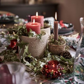 close up of a candle centrepiece on a festive table with real foliage red candles and pine cones