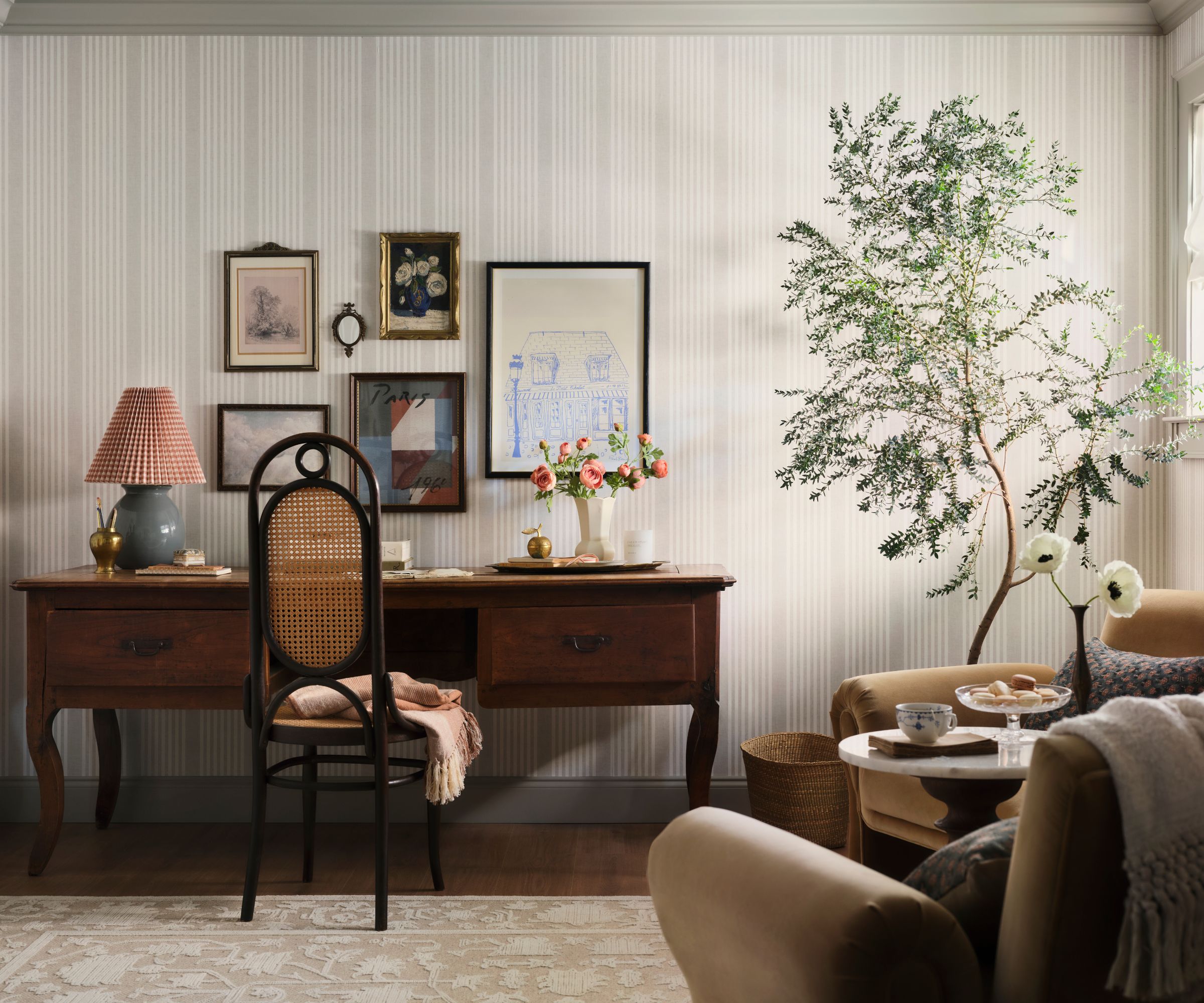 Home office with striped wallpaper, vintage wood desk, cane chair, potted plant, velvet armchairs and gallery wall