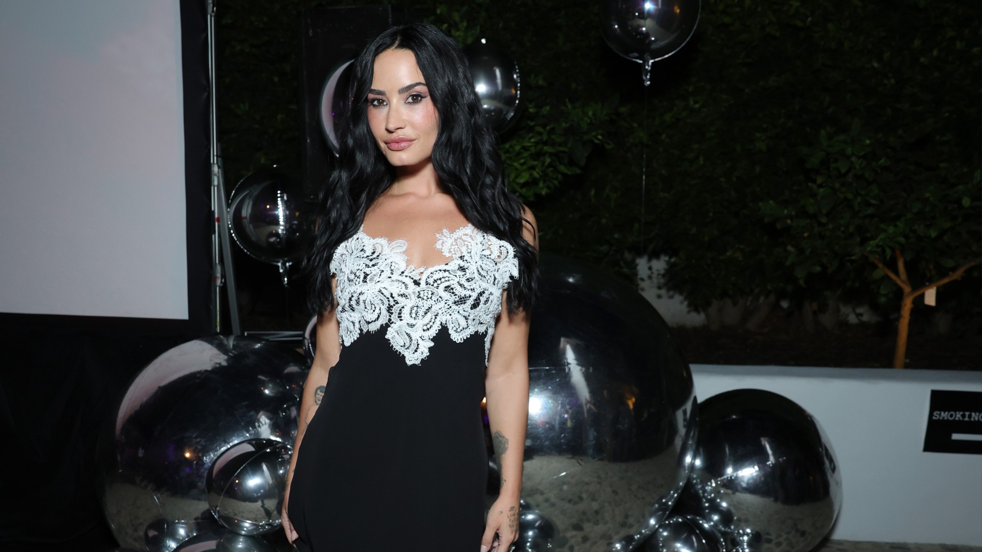 a woman with long, black hair wearing a black and white mini dress posing in front of silver balloons