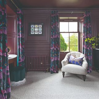A dark purple-painted room with light grey carpet and floral curtains decorating the windows