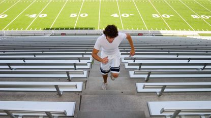 A high school football player runs the stairs in a football stadium.
