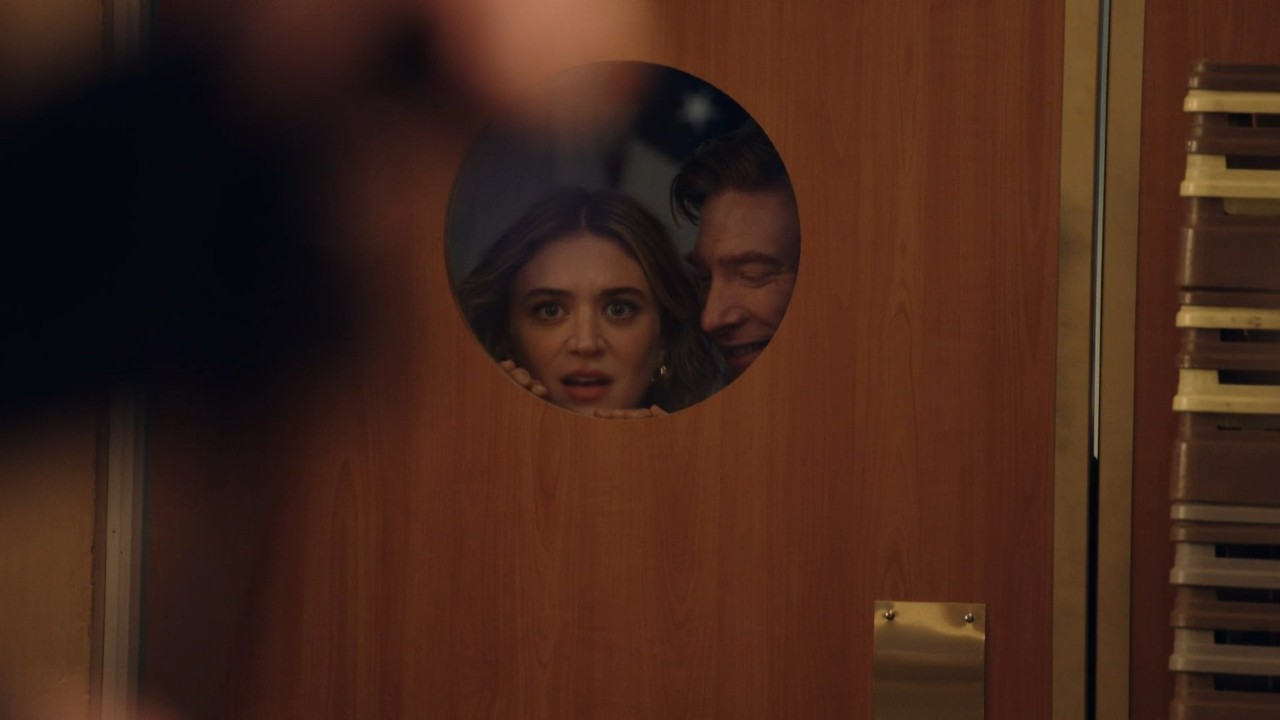 Domhnall Gleeson ve Chelsea Frei kağıttaki kapı penceresinden bakıyorlar.