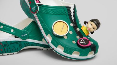 Squid Game Crocs piled on top of each other against a gray background, with Red Light Green Light Girl Jibbitz staring out into the foreground