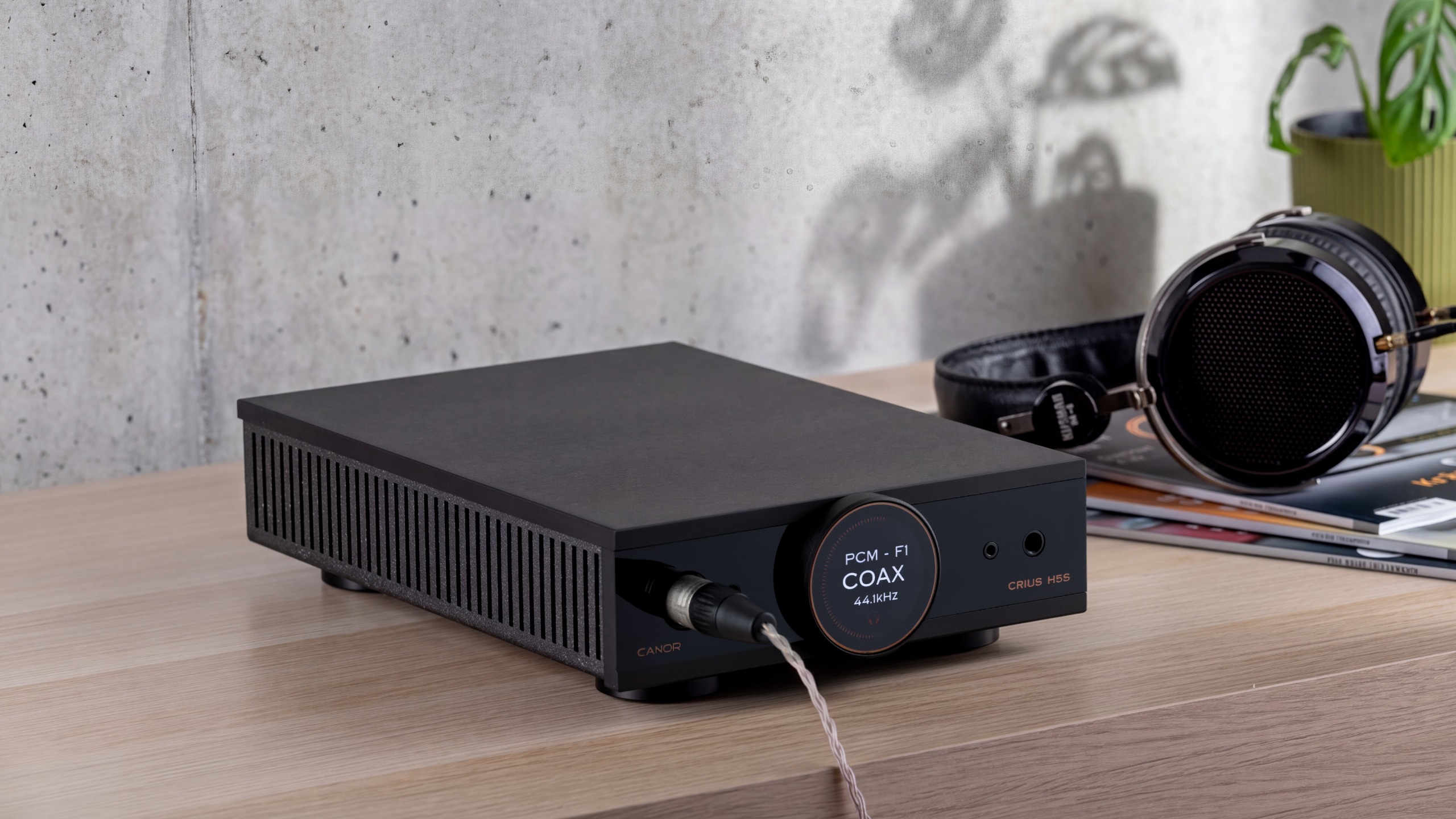 Canor Crius H5S DAC/headphone amplifier on a wooden surface next to a pair of headphones