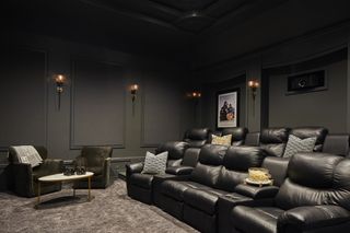 movie room with movie theater style seats, gray carpet, wall lights, green walls, green velvet armchairs, coffee table, cushions, artwork