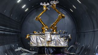 a cube-shaped satellite with two multi-jointed arms inside a cleanroom