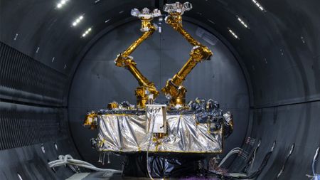a cube-shaped satellite with two multi-jointed arms inside a cleanroom