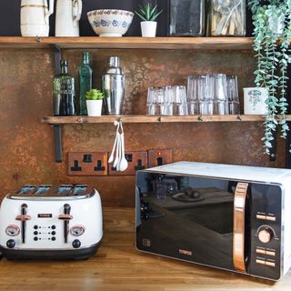 Microwave and toaster on wooden kitchen worktop with wooden shelving and crockery displayed in background