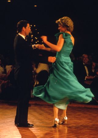 Princess Diana wearing a teal dress and silver heels twirling on a dance floor with Prince Charles, dressed in a tux