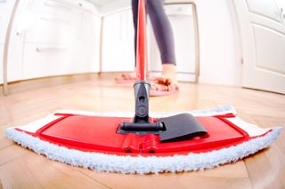 wide-view shot of a person cleaning a wooden floor with a dry mop, with feet in the background