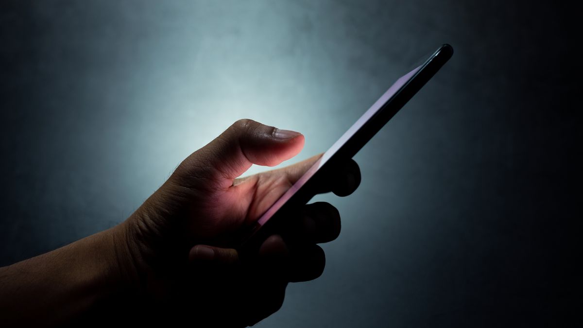 A hand holding a smartphone with dark background