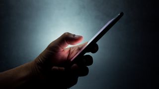 A hand holding a smartphone with dark background