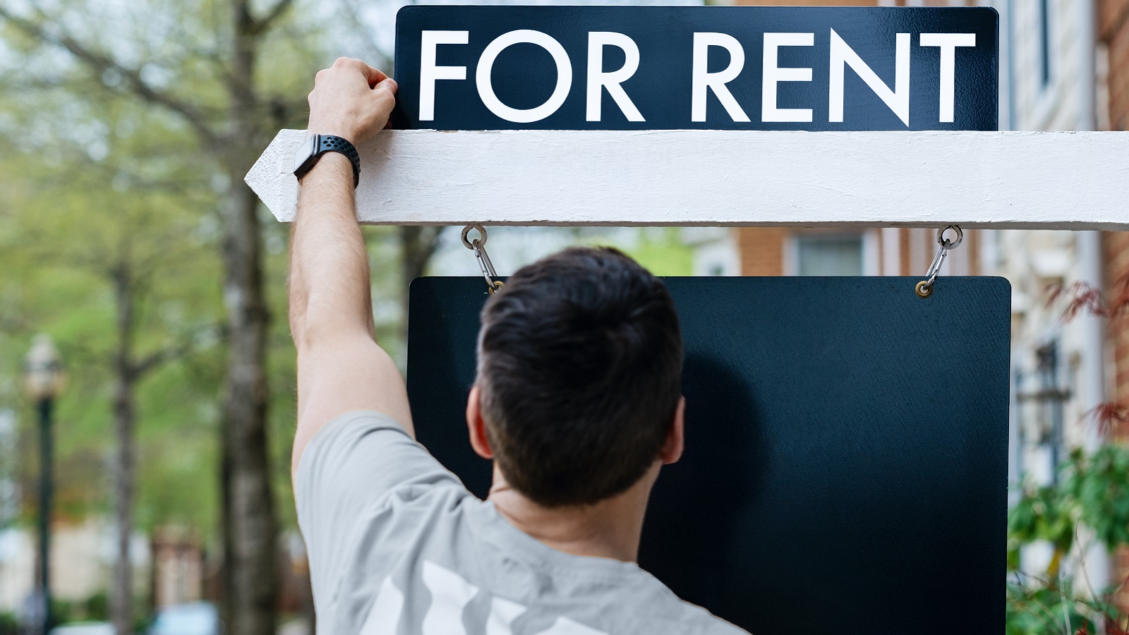 A man hangs a for rent sign outside a house.