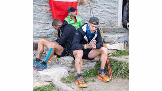 Ultra runner Galen Reynolds sits on stone steps with other runners, squeezing a hydration bottle.