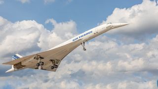 A photo of the Concorde plane flying with clouds in the background.