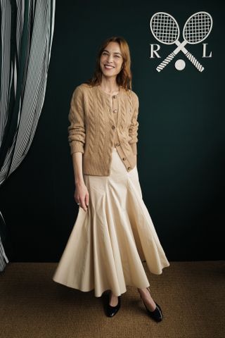 Alexa Chung wears a brown cardigan with a pleated midi skirt.