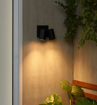 Black wall light casting yellow glow on an outdoor wall