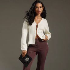 model wears white cardigan and brown cropped pants while holding a black clutch