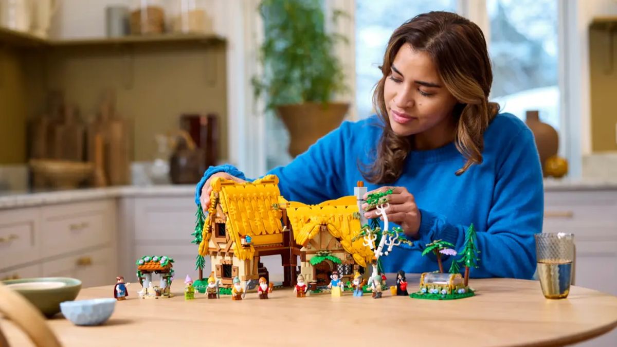 Lego Snow White and the Seven Dwarfs' Cottage set being positioned on a wooden table by a woman, with minifigures