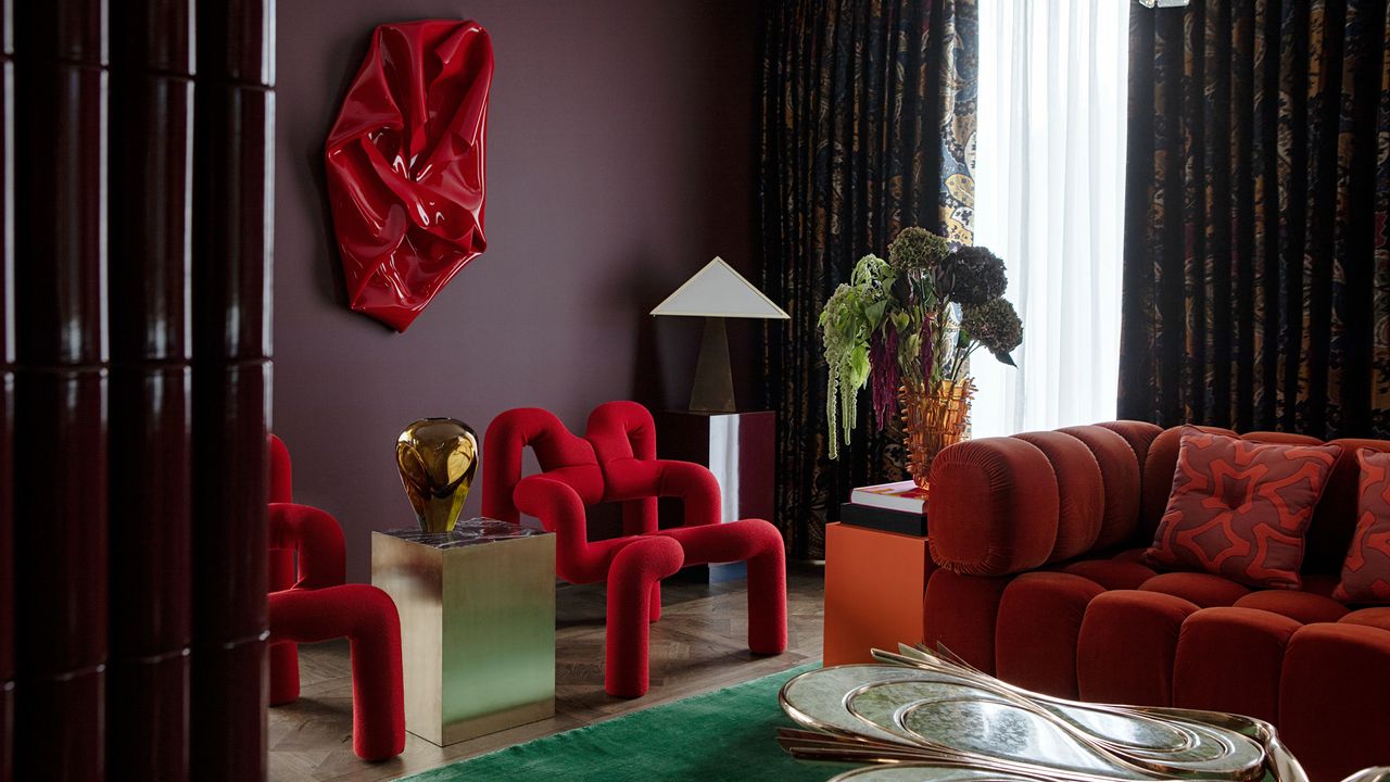 a dark purple living room with red chairs and an orange couch, with a green rug