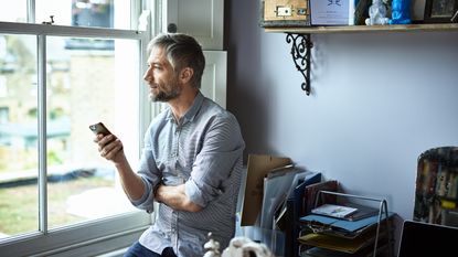 A man leans casually against his desk while talking to his financial adviser on his smartphone. 